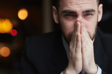 Portrait of modern bearded businessman looking at camera with red teary eyes, stressed and tired against black background, closing his mouth with hands