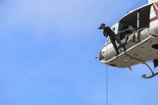 Soldier rappelling from helicopter in blue sky
