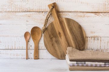 Wood round cutting board, spoons, stack of linen kitchen towels on white wood background, minimalistic, Provence, kinfolk