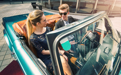 Young and attractive couple sitting in a luxurious retro cabriolet car