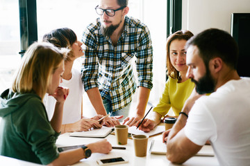 Obraz premium Group of digital marketing specialists is working on the new project concept by writing down all the ideas. Young managers are brainstorming during meeting on the new marketing promotion project.