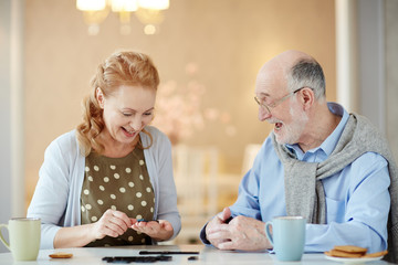 Portrait of cheerful mature couple laughing while enjoying playing domino at home 
