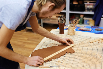 Young potter measuring piece of rolled clay