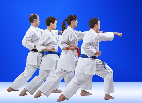 Four adult athletes are training punch on a light blue background