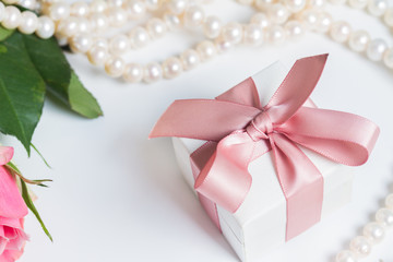 Gift box with pink ribbon with pearl jewellery on white table