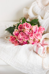 Female white dress and jewellery with freah roses bouquet and gift box on chair