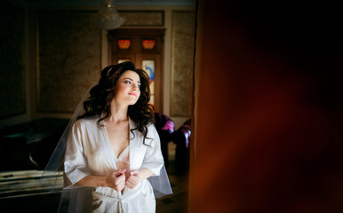 Stunning brunette bride opens her silk robe while she poses in the room