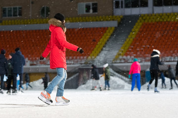 Woman in a red jacket on a skating rink  in the evening