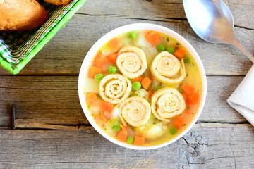 Home vegetable soup with omelet in a bowl. Rustic wooden background. Vegetarian soup with omelet, carrot, peas, leek, cauliflower and potatoes. Top view