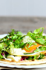 Crispy tortilla with fried egg, hummus and salad on a plate. Healthy and quick vegetarian tortilla recipe. Vertical photo. Closeup