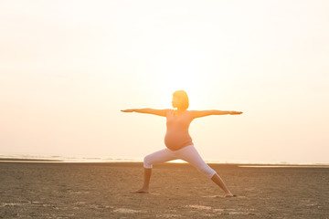 Fototapeta na wymiar silhouette of pregnant mother performing yoga on beach during sunset
