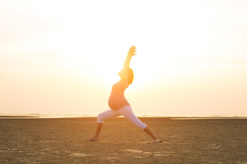 silhouette of pregnant mother performing yoga on beach during sunset
