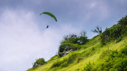 Paraglider flying off the Grassy Hills above Gunung Payung Beach, Bali