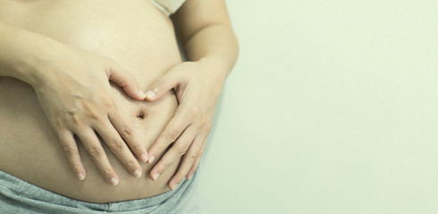 Closeup of Belly of a pregnant woman,pregnant woman holding her hands on her swollen belly shaping a heart, toned retro or vintage effect.selective focus