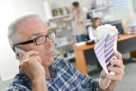 Man holding color charts, on telephone, bemused expresion