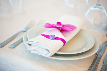 purple flower Decorated dinner napkin on white plates on a served wedding table