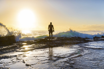 Silhouette of a person standing on a rock with ocean tide at sunrise
