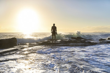 Silhouette of a person standing on a rock with ocean tide at sunrise - Powered by Adobe