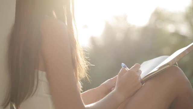 Woman sitting at balcony and writing in diary with garden on the background