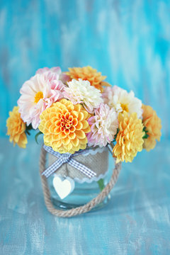 Beautiful bouquet of a yellow and pink dahlias in a glass vase on a blue background.