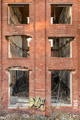 Outside wall of an abandoned brick building in an industrial area with deteriorated windows like a post apocalyptic  scene