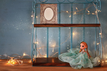 Cute doll and blank photo frame next to warm garland lights