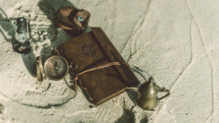 Antique compass and old collection pirate marine adventure items on sand beach.