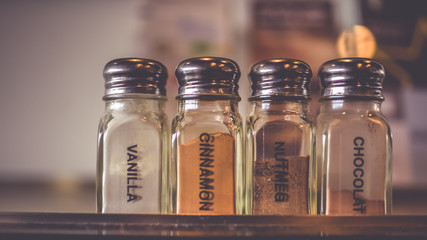 A vanilla powder, cinnamon powder, nutmeg powder and chocolate powder in glass bottle in vintage style picture.