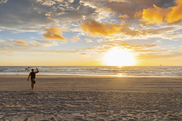 Surfer walking on the beach with surfboard on head at sunrise. Surfers Paradise, Gold Coast.