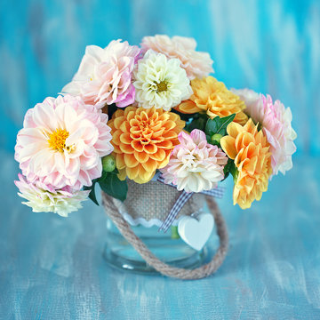 Beautiful bouquet of a yellow and pink dahlias in a glass vase on a blue background.