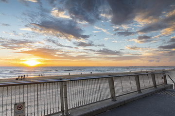 People walking on the beach at Surfers Paradise Gold Coast, with colourful sunrise in horizon