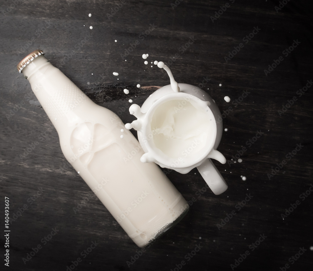 Wall mural Milk splash and bottle milk on dark wooden table,Top view