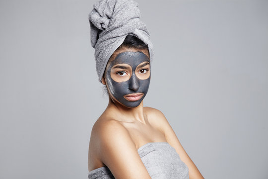 serious woman making facial treatment. clay facial grey mask