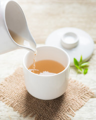 Pouring tea from jug to cup of tea and tea leaves on wooden