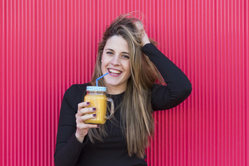 portrait of a beautiful young woman holding a healthy jug of orange juice. Red background