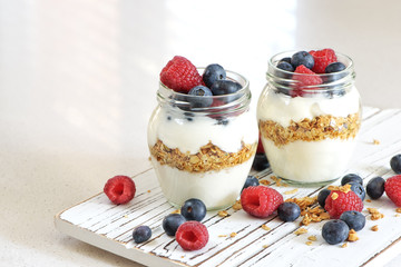 Yogurt with bluberry and raspberry in the glass jars with berries around on the wooden board