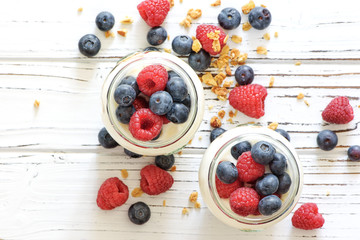 Yogurt with bluberry and raspberry in the glass jars with berries around on the wooden board