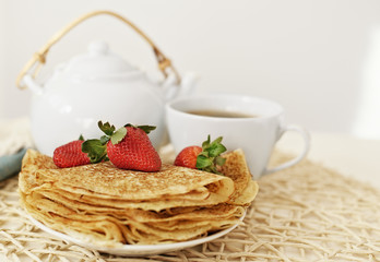 Pancakes with a strawberry and hot tea in the teapot and cup
