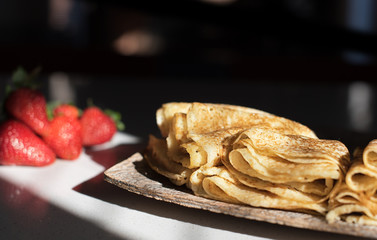 Pancakes on the wooden plate stay on the table with sunlight from window on them