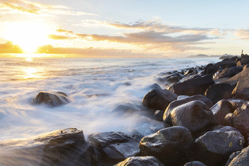 A person watching the sunrise and ocean tide rushing over the rocks at Bureleigh Heads Gold Coast.