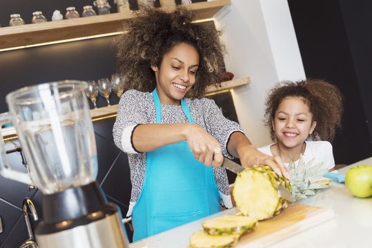 Beautiful African American Woman And Her Daughter Cutting Fruit In The Kitchen 