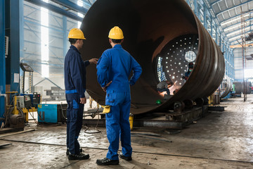 Workers supervising the manufacture of a metallic cylinder