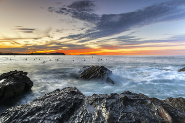 Colourful sunset with waves lashing up against a large rock in the ocean at Currumbin Rock Gold Coast
