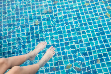 Girl feet in swimming pool on a hot summer day