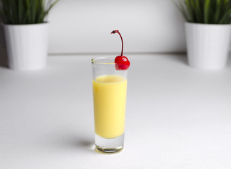 Yellow cocktail in a glass with a cherry on a white background