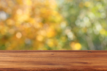 Naklejka na ściany i meble An empty wooden table on a background of autumn trees. The background is blurred.