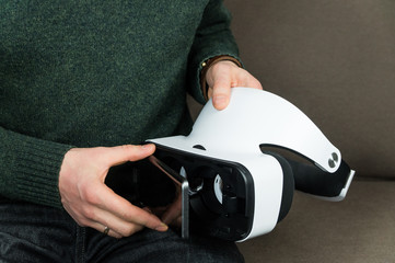 Attaching smartphone to virtual reality headset. Close-up image of hands holding vr glasses and connecting mobile phone to them