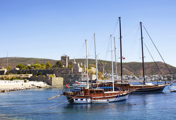 Luxury yachts (sailing boats) parked on turquoise water in front of Bodrum castle. The image shows Aegean and Mediterranean culture of coastel lifestyle.