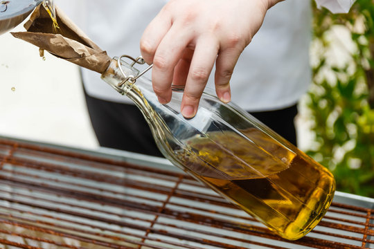 Chef Pouring Rosemary Oil From Pan in The Glass Bottle with Paper Cone.