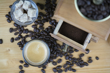 Coffee grinder with espresso and sugar cubes served in small glasses viewed from above with focus to the open drawer with ground beans